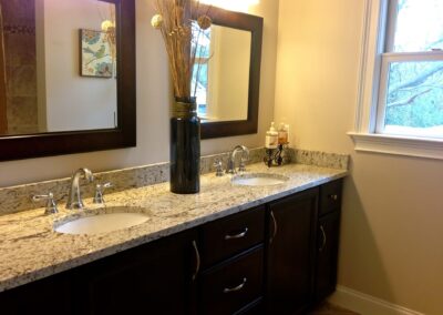 Modern bathroom with double sink vanity, granite countertop, dark wooden cabinets, vase with tall decor, and wall-mounted mirror. - Milton GA by Simone Feldman Designs