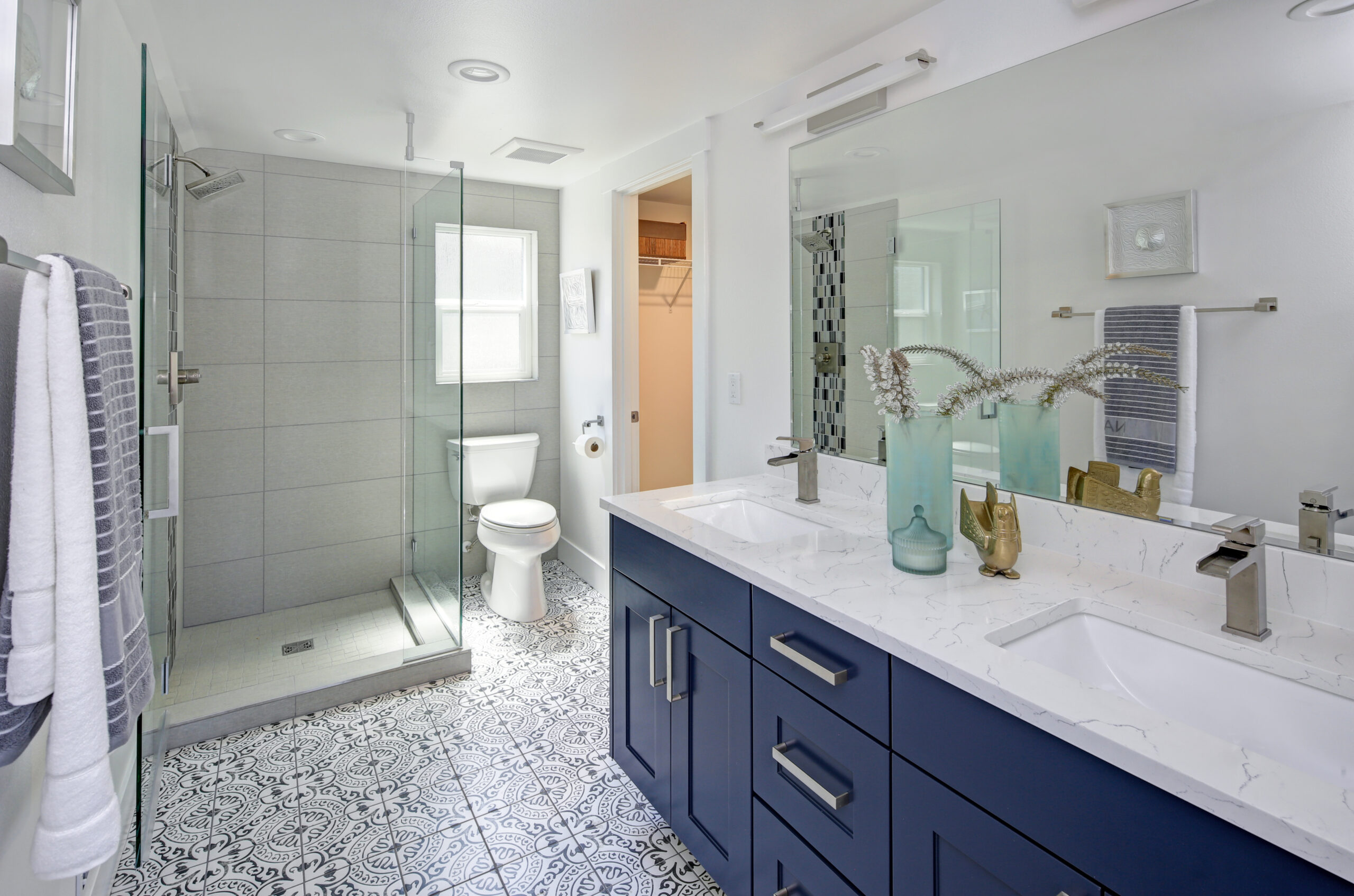 Modern bathroom with blue cabinets, marble countertop, glass shower, patterned tile floor, and stylish decor.