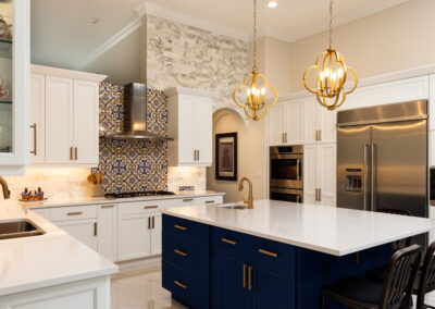 Modern kitchen with white cabinets, blue island, gold fixtures, stainless steel appliances, and patterned backsplash.