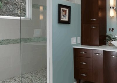 Modern bathroom with turquoise walls, glass walk-in shower, pebble tile floor, dark wood vanity, and pendant lighting. Milton, GA by Simone Feldman Designs