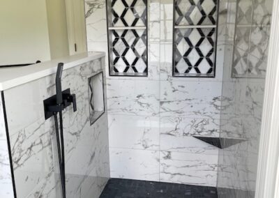 Luxury bathroom shower with white marble walls, black geometric tile accents, sleek black fixtures, and dark tiled floor.
