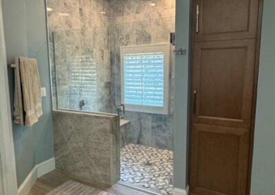 Modern bathroom with marble shower tiles, glass door, wooden cabinet, towel rack, and stylish flooring under soft lighting.