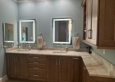 Modern bathroom with wooden cabinets, dual mirrors, soft gray walls, ambient lighting, beige countertop, and striped rug.