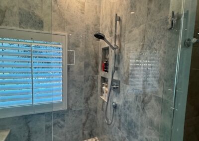 Luxurious marble shower with glass doors, rainfall showerhead, built-in shelves, gray tile walls, and geometric floor tiles.