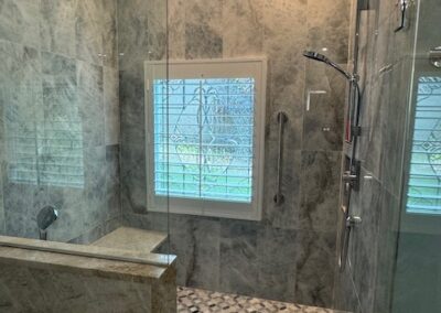 Modern marble-tiled bathroom with glass shower, rainfall showerhead, handheld shower, and patterned tile floor by Simone.