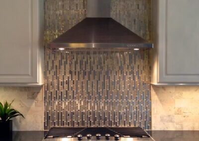 Modern kitchen with stainless steel range hood, mosaic tile backsplash, white cabinets, and black countertop. - Alpharetta GA by Simone Feldman Designs