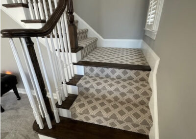 Elegant staircase with dark wood steps, patterned carpet runner, white railing, and soft gray walls in a modern interior.
