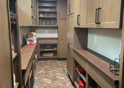 Modern pantry with wooden cabinets, herringbone tile floor, open shelves, glassware, and neatly organized storage baskets.
