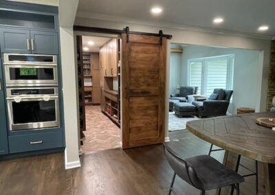 Modern kitchen with blue cabinets, double wall ovens, hardwood floors, barn door leading to pantry, and cozy living area.
