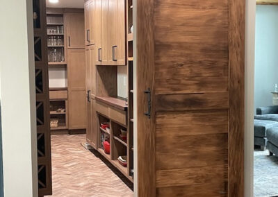 Rustic wooden sliding barn door opening to a modern pantry with herringbone tile floor, custom cabinets, and wine storage.