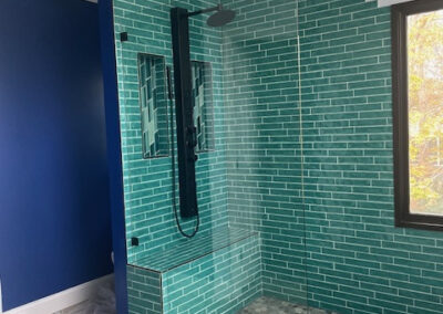 Modern bathroom with teal subway tile shower, black rain showerhead, glass door, hexagon floor tiles, and blue walls. - Johns Creek GA by Simone Feldman Designs