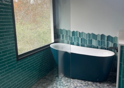 Modern bathroom with teal tiles, freestanding navy bathtub, glass shower, and hexagonal floor tiles overlooking nature. Alpharetta GA by Simone Feldman Designs