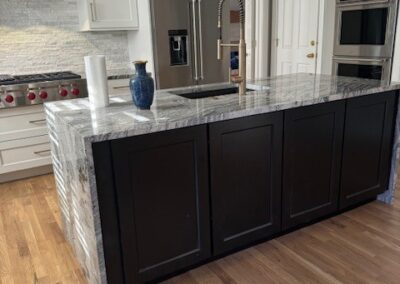 Modern kitchen with black island, granite countertop, stainless steel appliances, white cabinetry, and wood floors. - Milton GA by Simone Feldman Designs