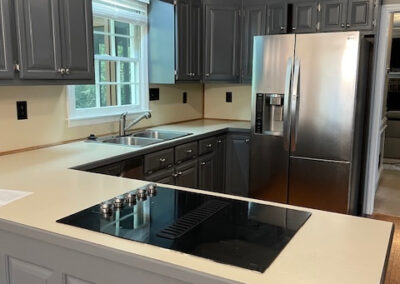 Modern kitchen with gray cabinets, stainless steel fridge, electric stovetop, and natural light coming from a window. Roswell GA by Simone Feldman Designs